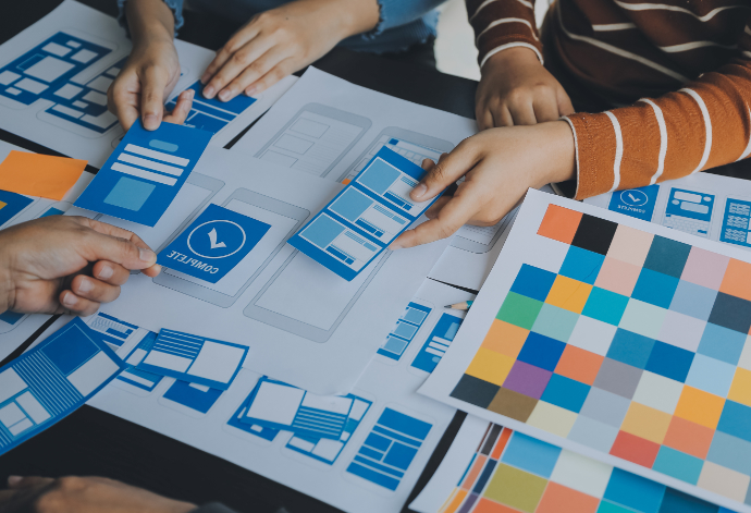 Overhead view of 3 people at a desk working on some cut-out paper wireframes and colour swatches